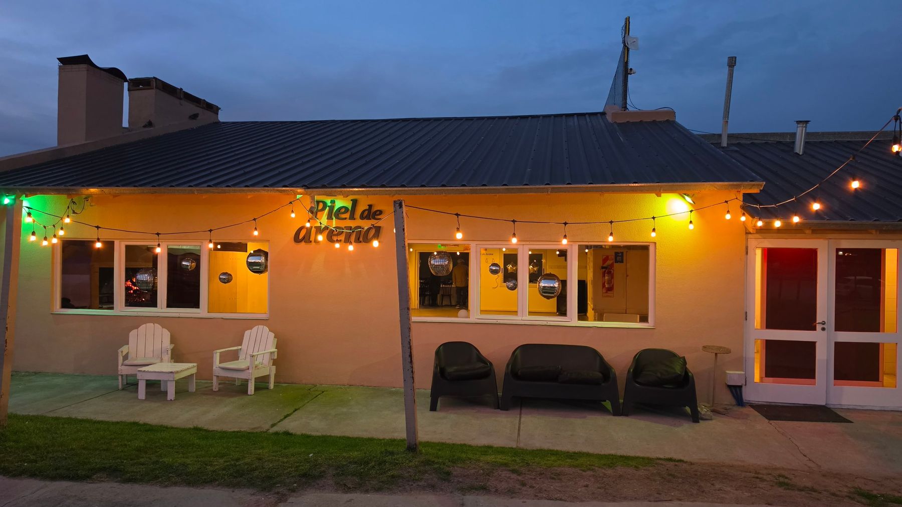 Fachada de Piel de Arena al atardecer, con guirnaldas de luces y livings en la galería