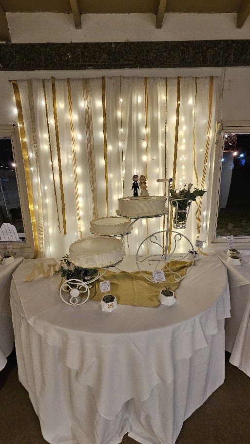 Mesa de torta de casamiento de tres pisos frente a una cortina de luces y cintas doradas