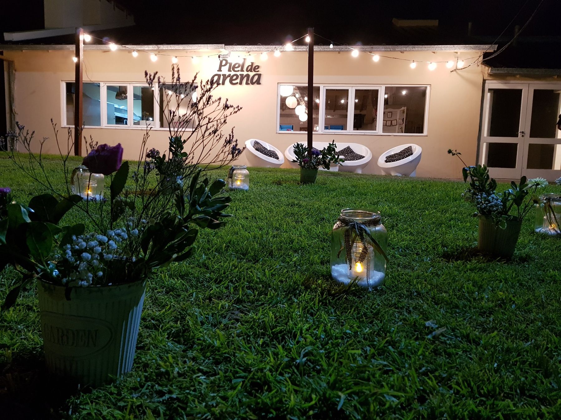 Jardín de noche con frascos con velas, flores y guirnaldas de luces frente al salón