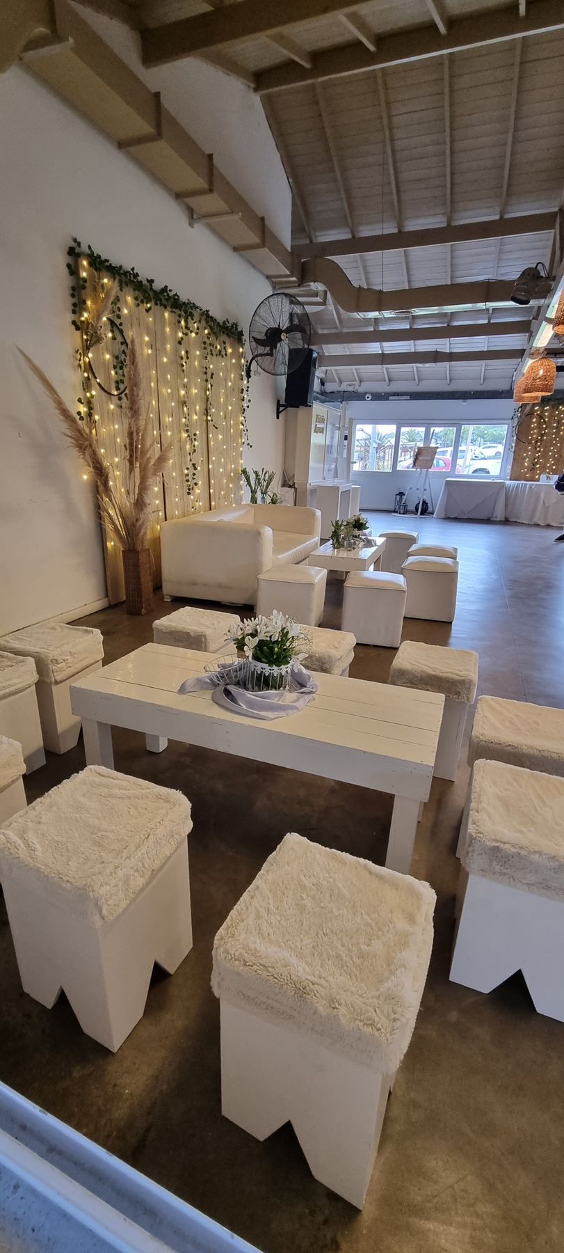 Living blanco con puffs de piel, mesa baja y panel de luces con enredadera