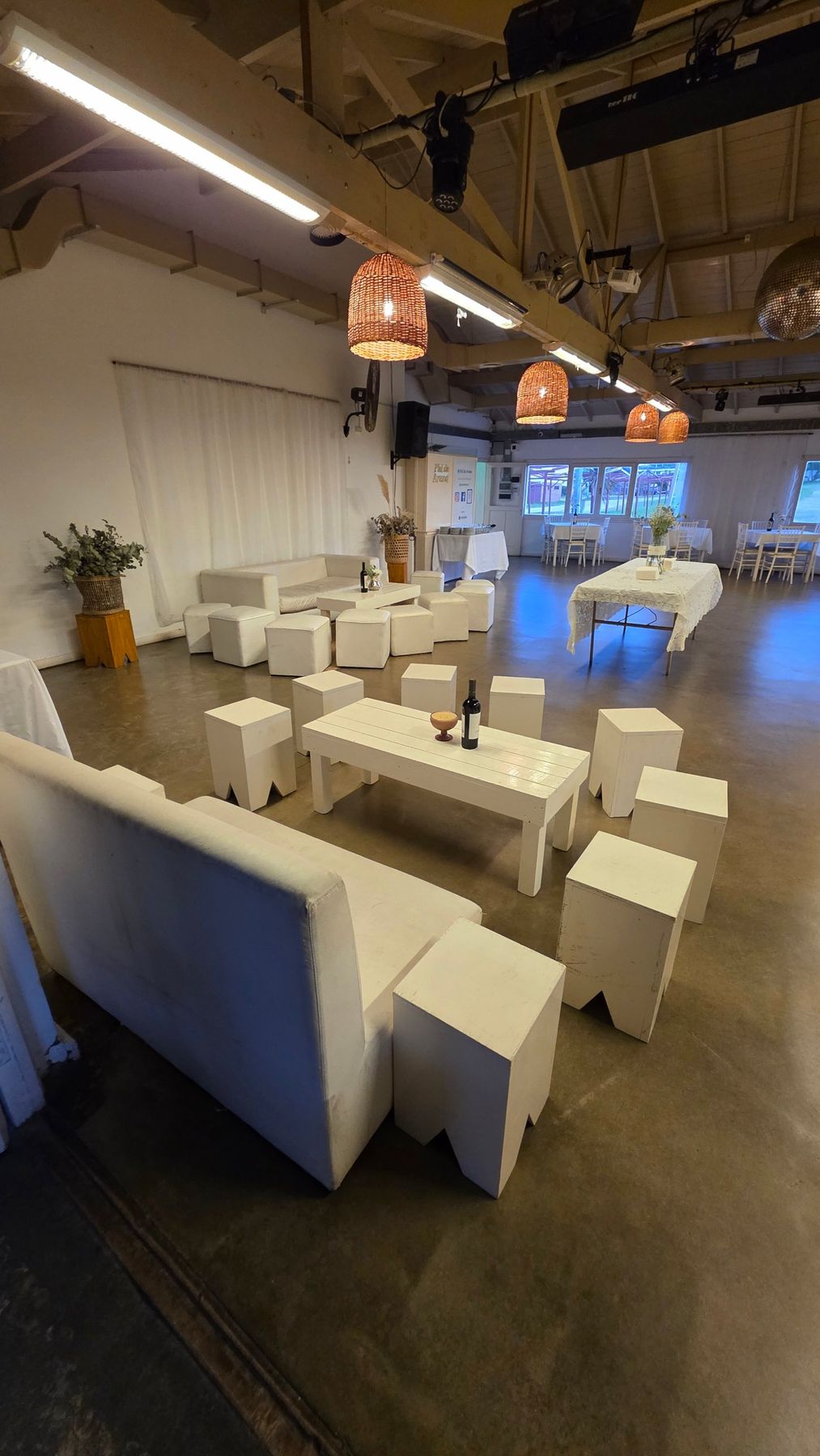 Salón armado con livings blancos, banquetas y mesas con sillas Tiffany junto al ventanal