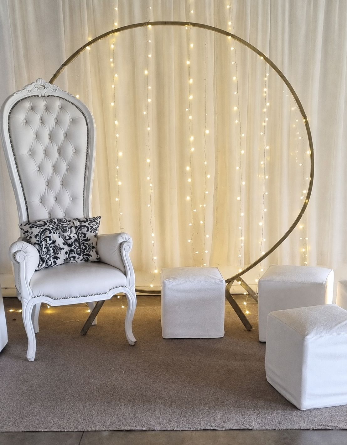 Sillón trono blanco capitoné junto a un aro dorado con cortina de luces