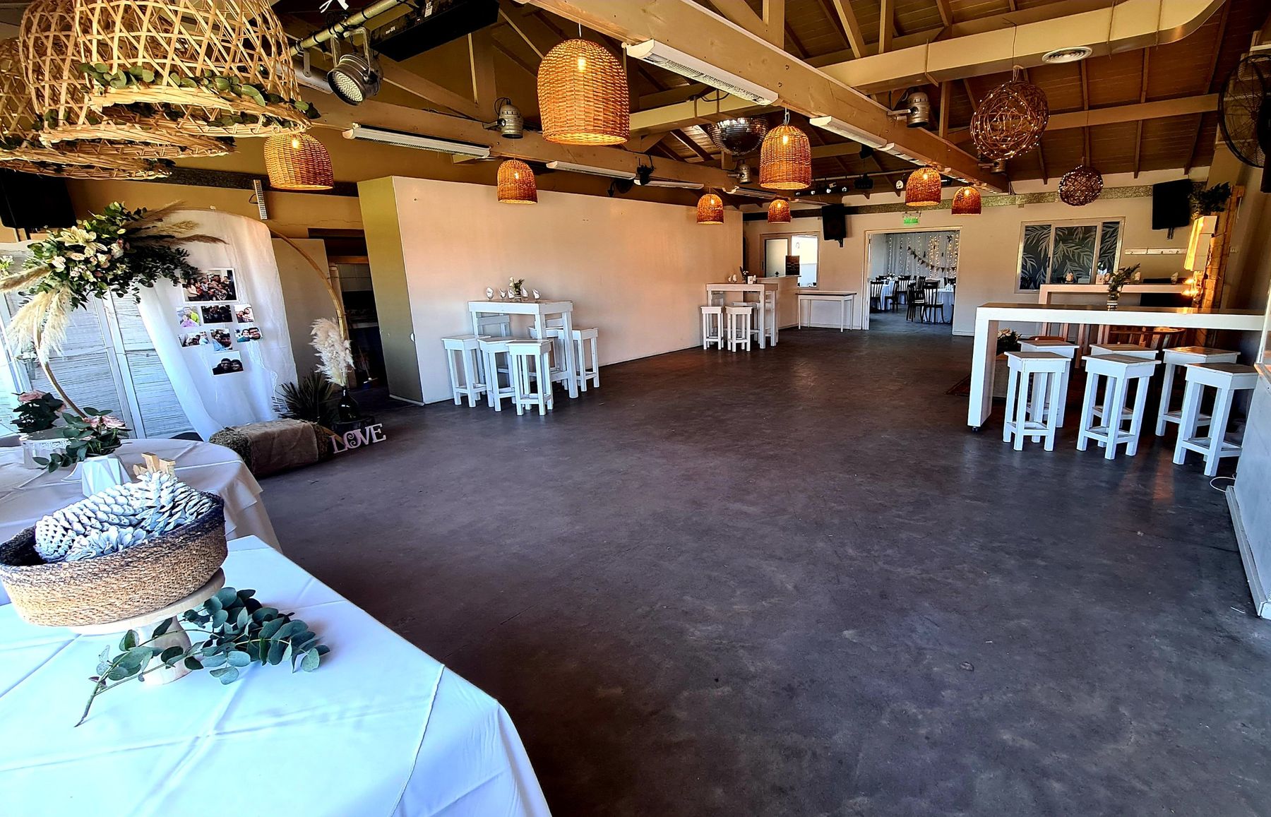 Salón amplio con lámparas de mimbre, barras altas blancas y mesa de recepción decorada