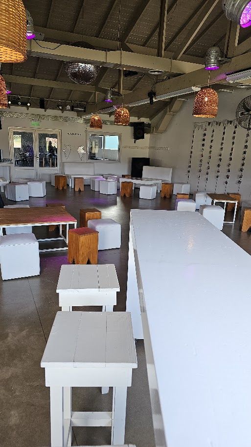 Salón con mesas largas blancas, puffs y lámparas de mimbre