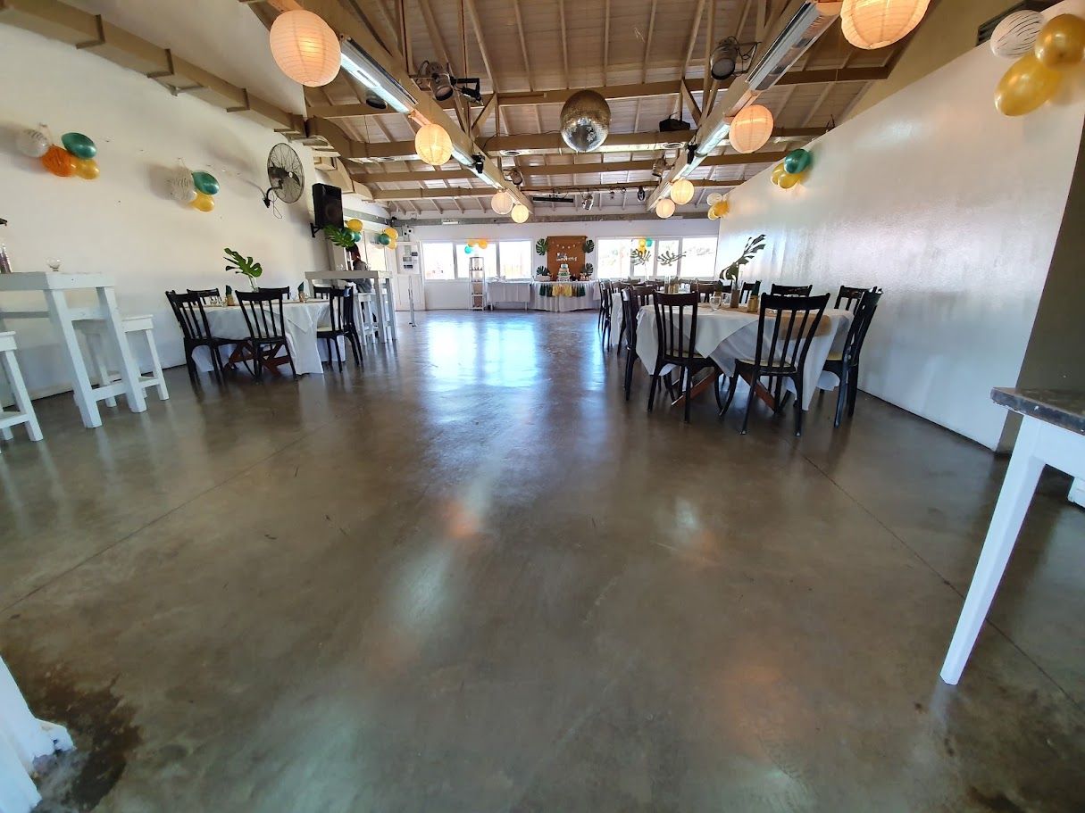 Salón amplio con mesas armadas, barras altas y globos dorados y verdes