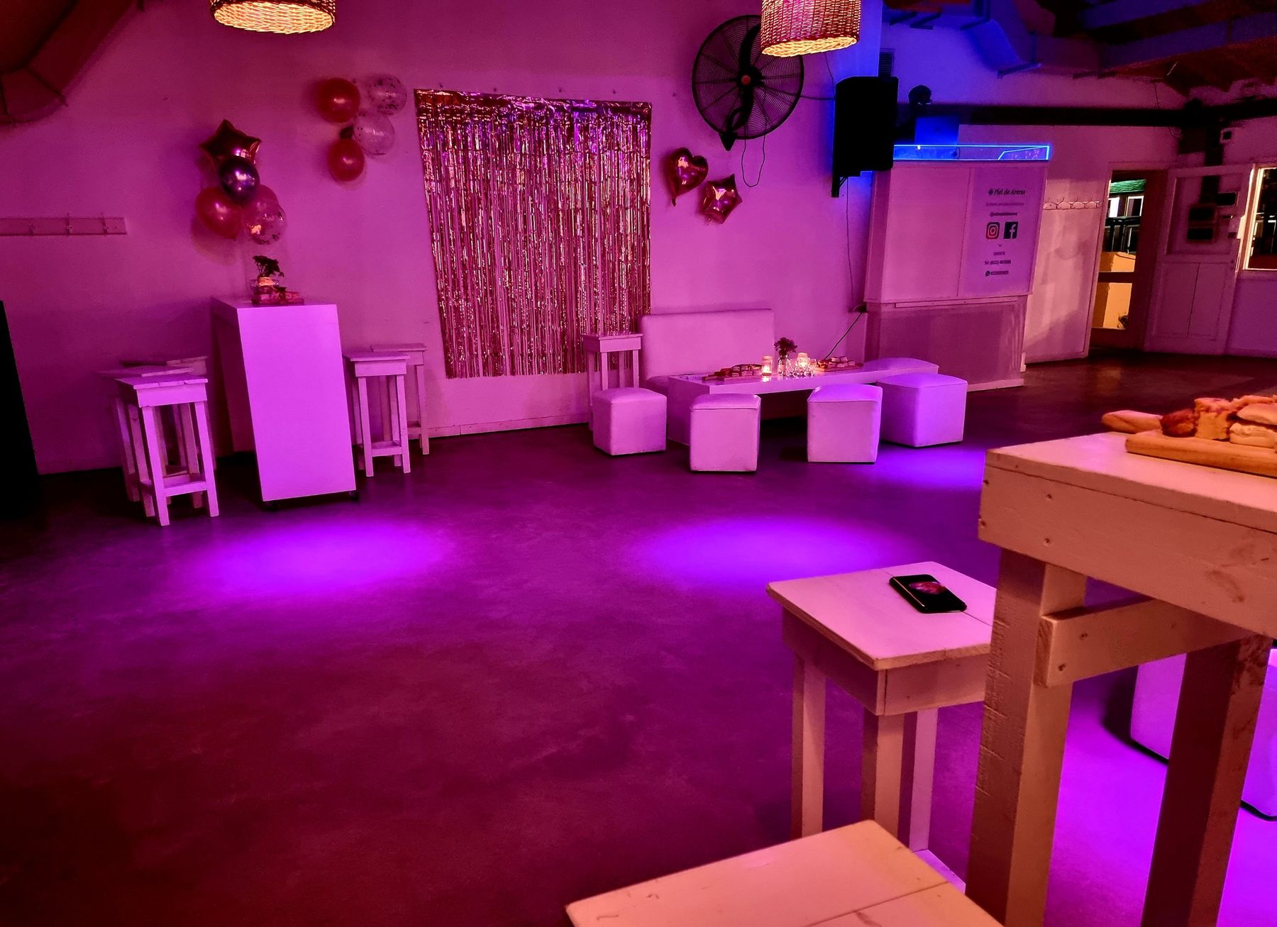 Rincón con living blanco, cortina metalizada y globos, iluminado en rosa