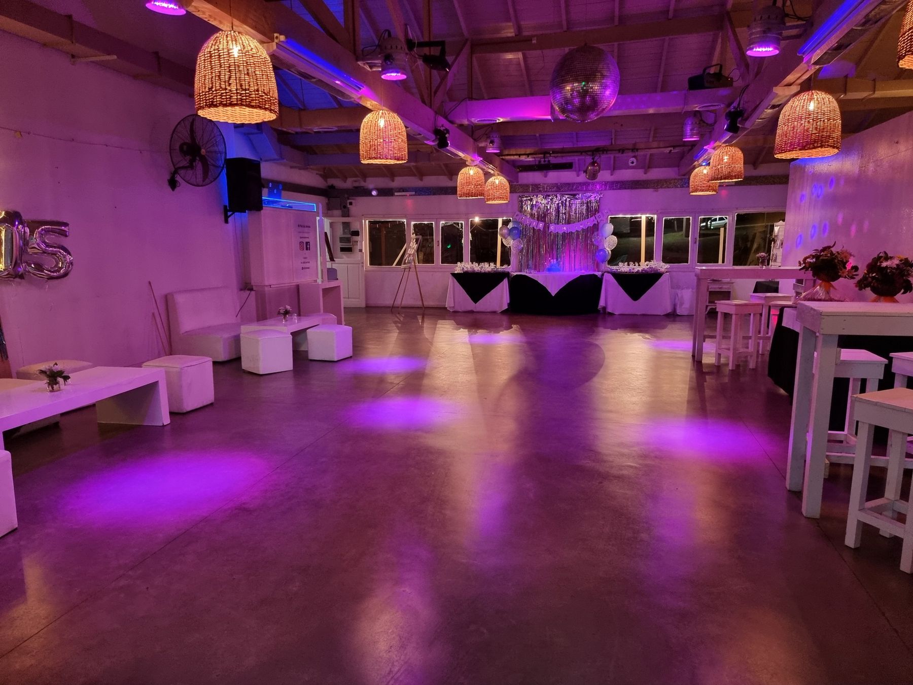 Pista de baile con bola de espejos, lámparas de mimbre y livings, iluminada en violeta