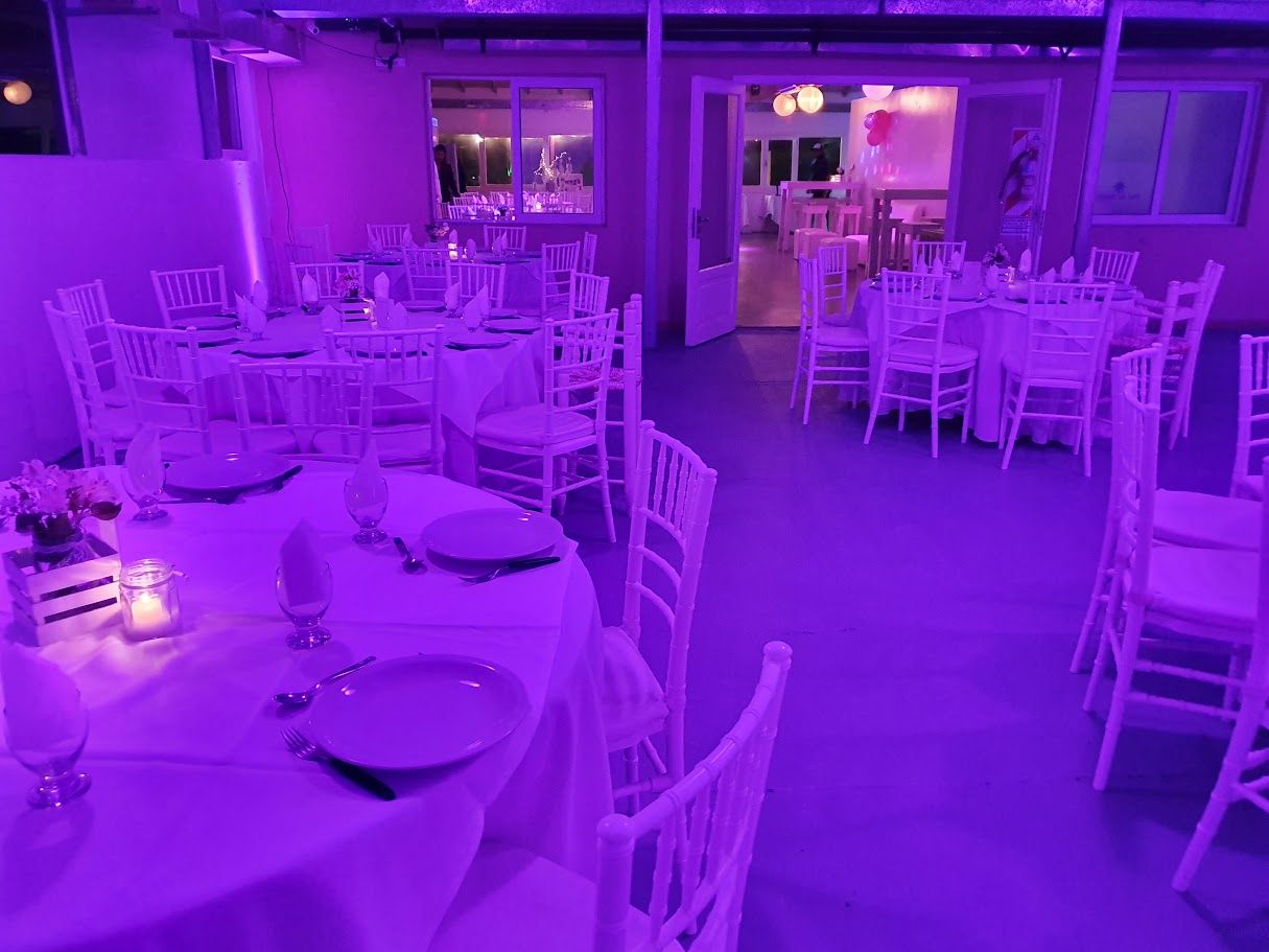 Salón con mesas redondas y sillas Tiffany blancas, iluminado en violeta